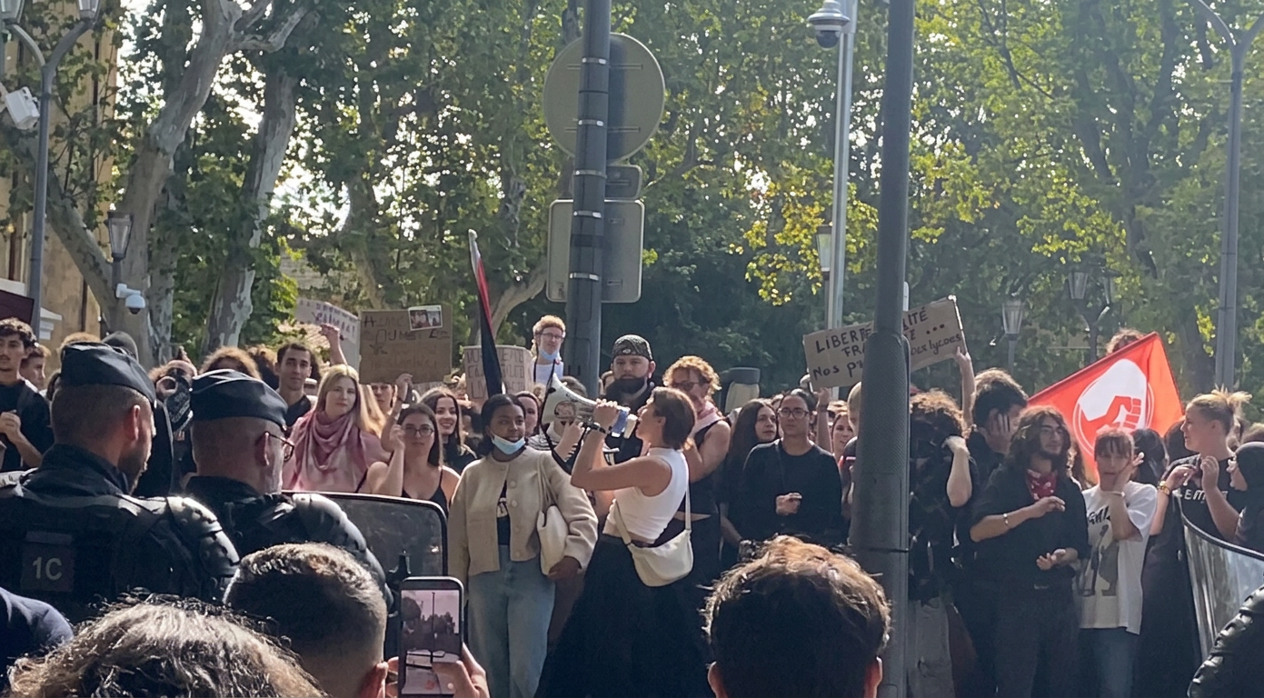 Gençlerin bir protestoda toplandığı, ön planda bir kadının megafonla konuştuğu kalabalık bir grup.